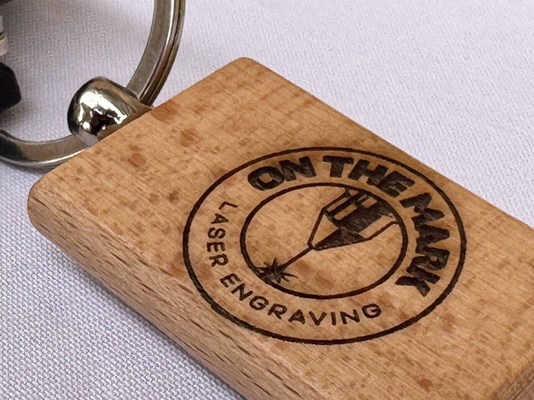 Wooden keychain engraved with the On The Mark logo
